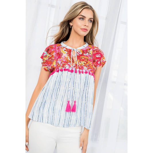 Woman wearing vibrant mixed print babydoll top with paisley and stripes, hot pink tassel details, and tie neckline